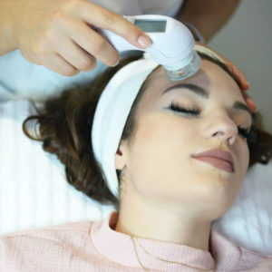 Tratamiento facial con dispositivo Wishpro en la frente de una mujer joven durante sesión estética