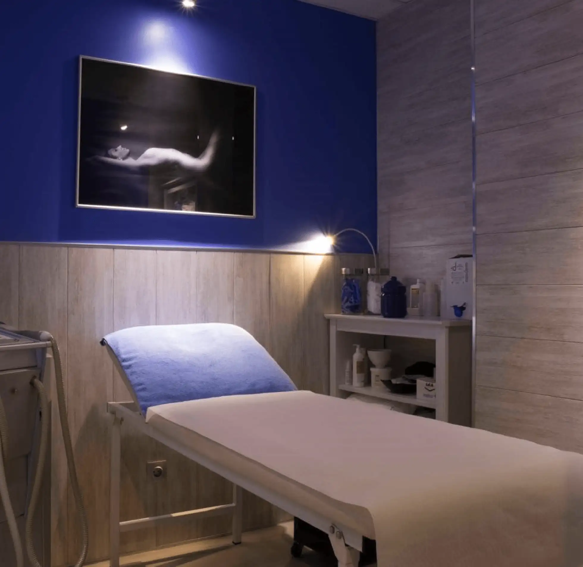 Habitación de un centro de estética con una camilla, paredes de color azul y un cuadro en la pared.