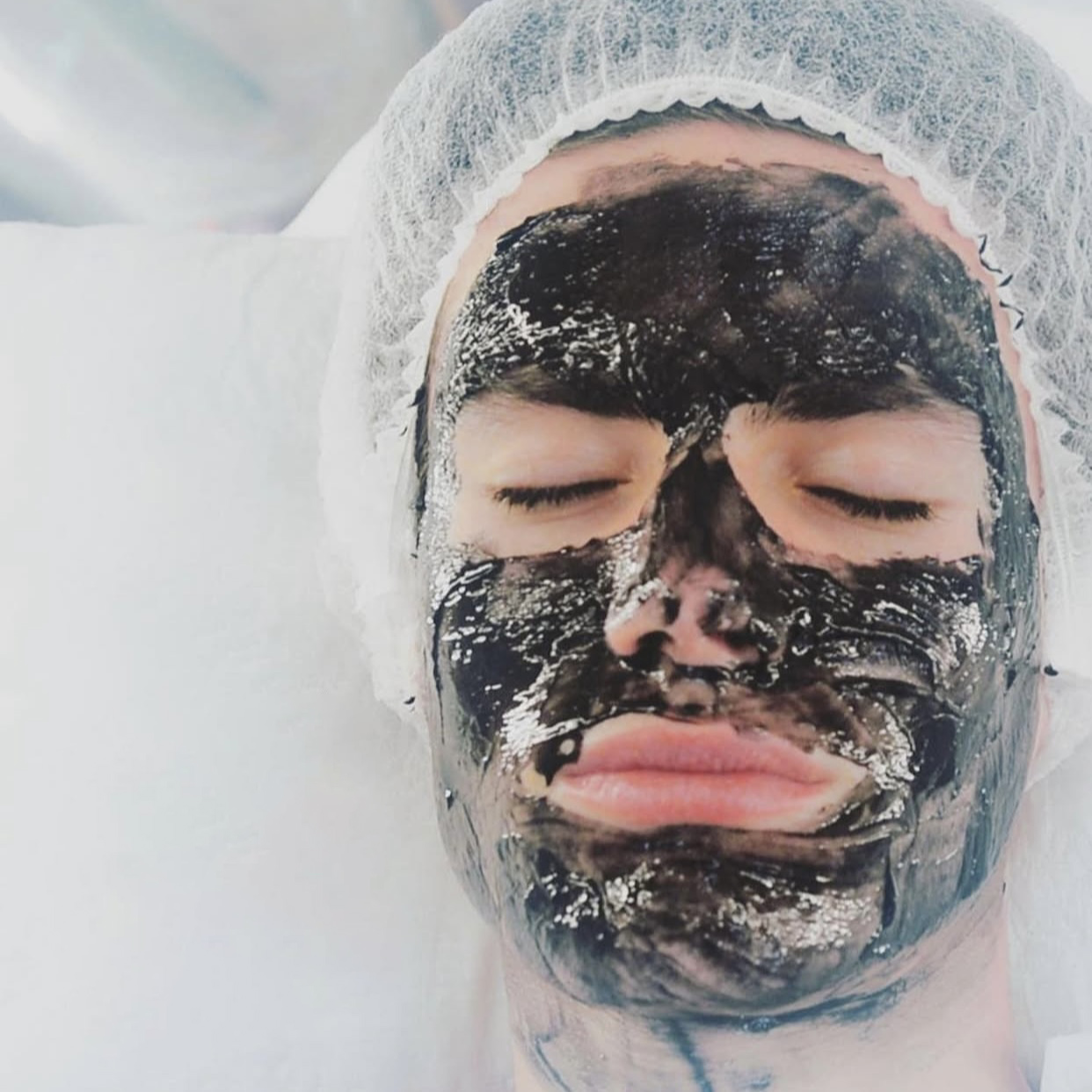 Rostro de una persona con los ojos cerrados durante la aplicación de una mascarilla facial negra.
