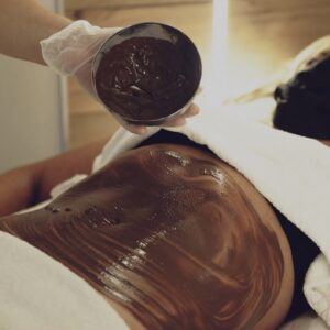Aplicación de envoltura corporal en el abdomen de una clienta utilizando un producto cosmético de textura densa.