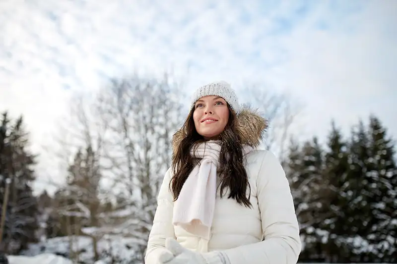 Mujer con ropa de abrigo en un paisaje nevado, ilustrando la recomendación de realizar tratamientos faciales y corporales en invierno por la baja exposición solar.
